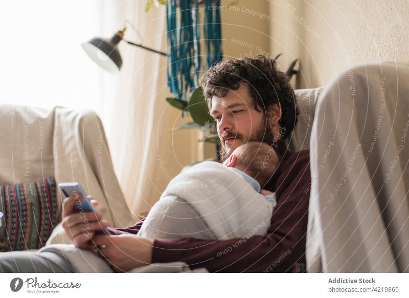 Father with unrecognizable newborn baby chatting on smartphone at home dad spare time embrace fatherhood internet using gadget man device cellphone