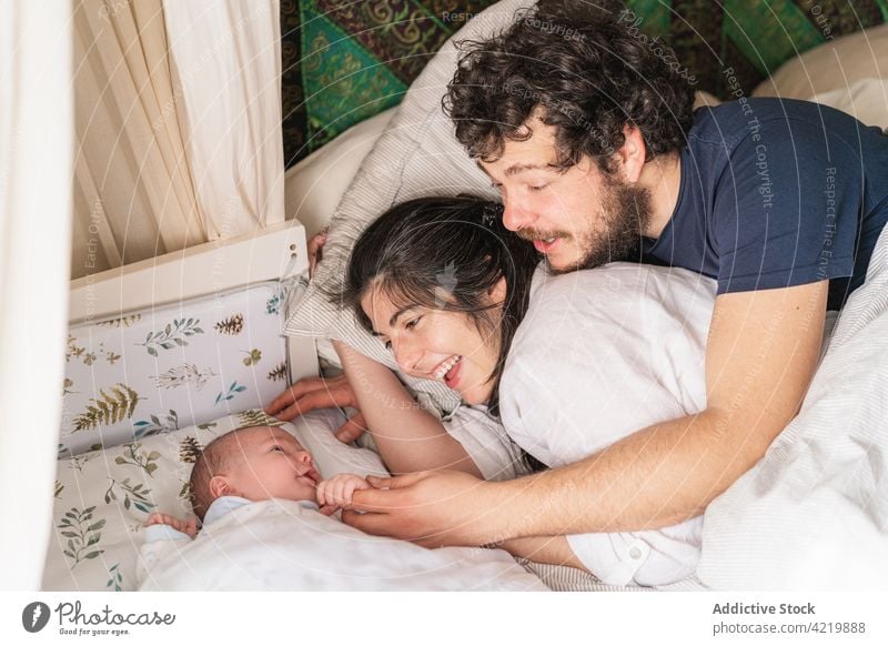 Smiling family with newborn baby resting in bed interact parenthood babyhood cheerful spend time home idyllic father mother husband wife mom dad enjoy content