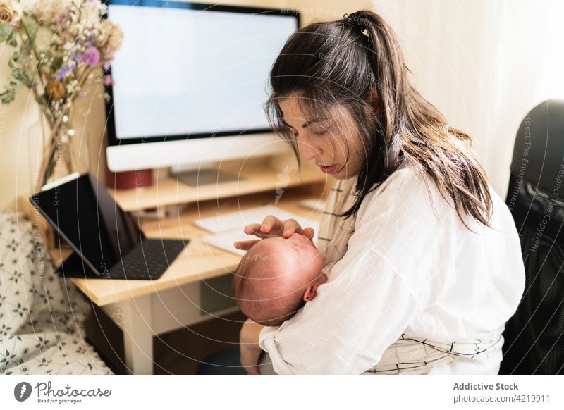 Mom holding baby and working on computer at home woman freelance newborn motherhood multitask desk notebook flower bonding write busy infant using study embrace