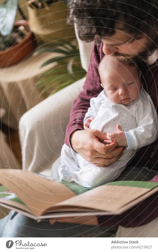 Father with newborn baby reading book at home dad fatherhood literature spend time armchair house man infant babyhood charming idyllic innocent legs crossed sit