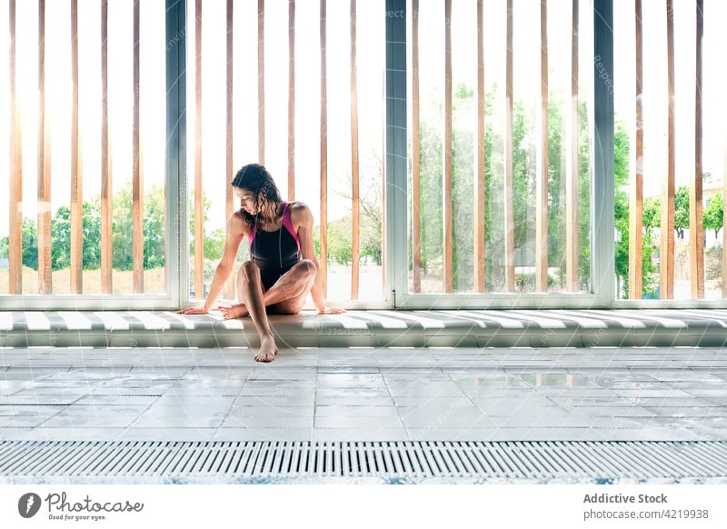 Swimmer in swimsuit resting against windows after working out swimmer legs crossed sport break lonely professional body woman tile floor wistful alone ribbed