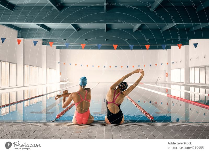 Unrecognizable swimmers warming up against pool in building warm up sport stretch workout training wellness body women together swimwear sit poolside