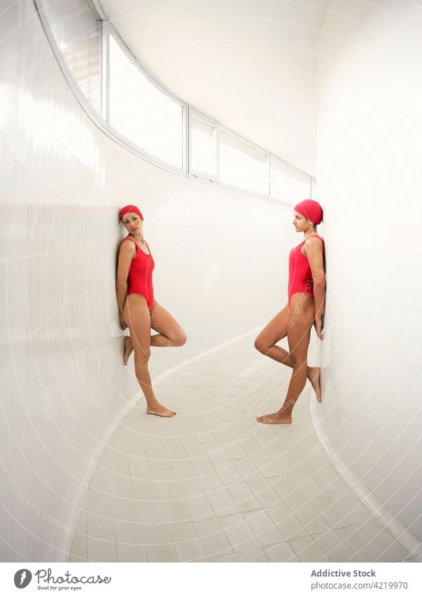 Swimmers in swimsuits leaning on walls in corridor athlete swimwear leg raised sport duo body hand behind back professional women curve window tile floor