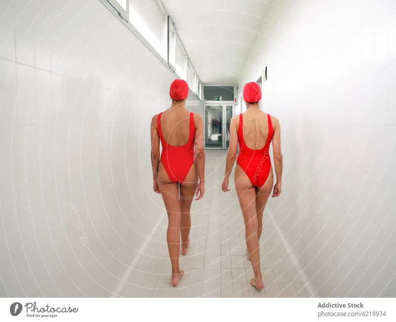 Unrecognizable sportswomen in swimsuits walking in hallway swimmer swimwear girlfriend friendship sporty body duo athlete hug interact corridor professional
