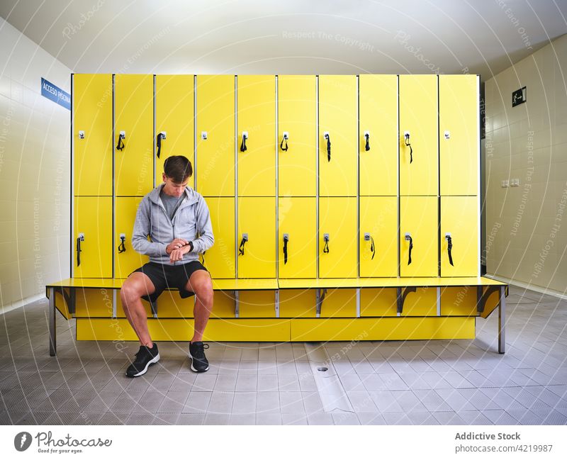 Sportsman watching time on wristwatch in locker room sportsman check up punctual bench style modern sneakers sportswear sit attentive hallway floor row similar