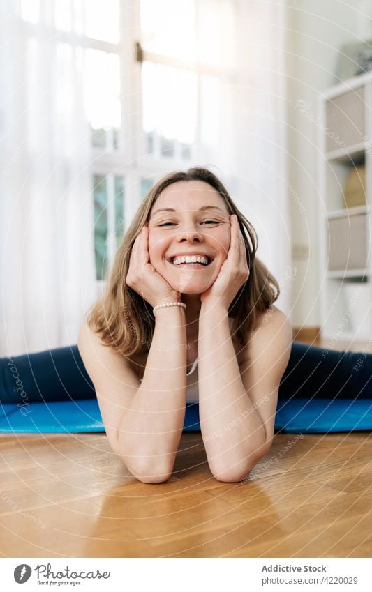 Content woman sitting in Split yoga pose and looking at camera split practice stretch flexible asana home smile female cheerful harmony fit content healthy mat