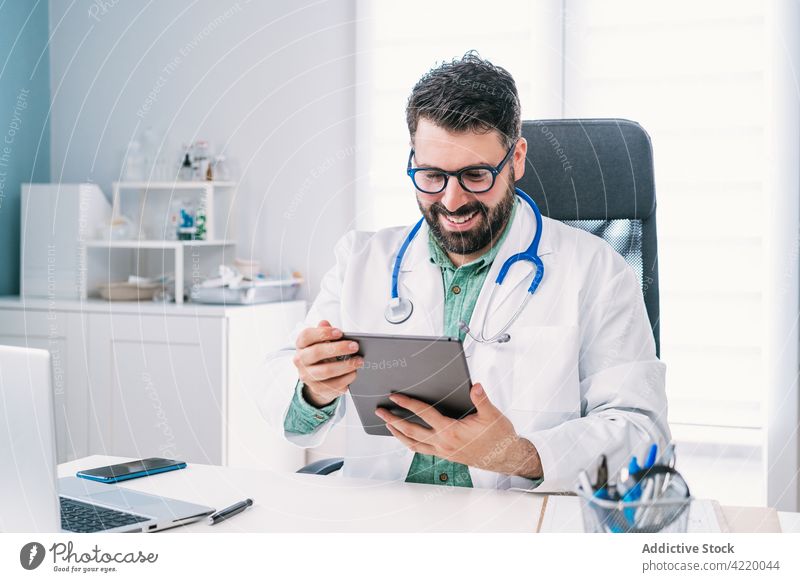 Smiling physician with tablet during video call in clinic smile talk internet online man hospital using gadget device video chat speak cheerful laptop