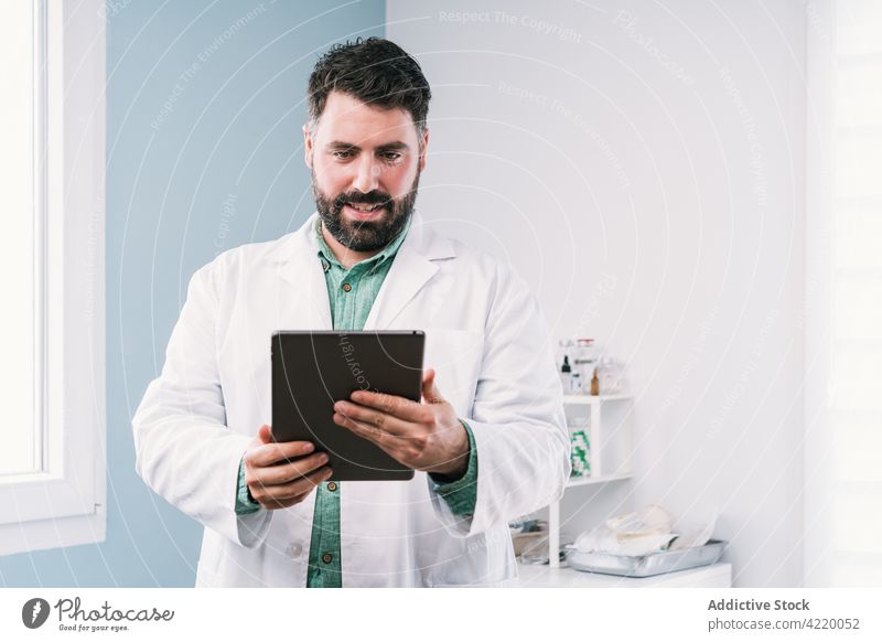 Doctor in uniform working on tablet in hospital man professional internet online clinic using gadget device doctor surfing watching attentive browsing focus