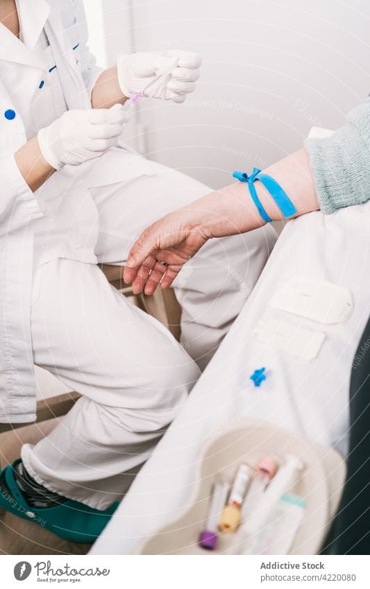 Crop nurse preparing patient for intravenous drip in clinic medical procedure prepare health care tourniquet uniform hospital professional glove sterile
