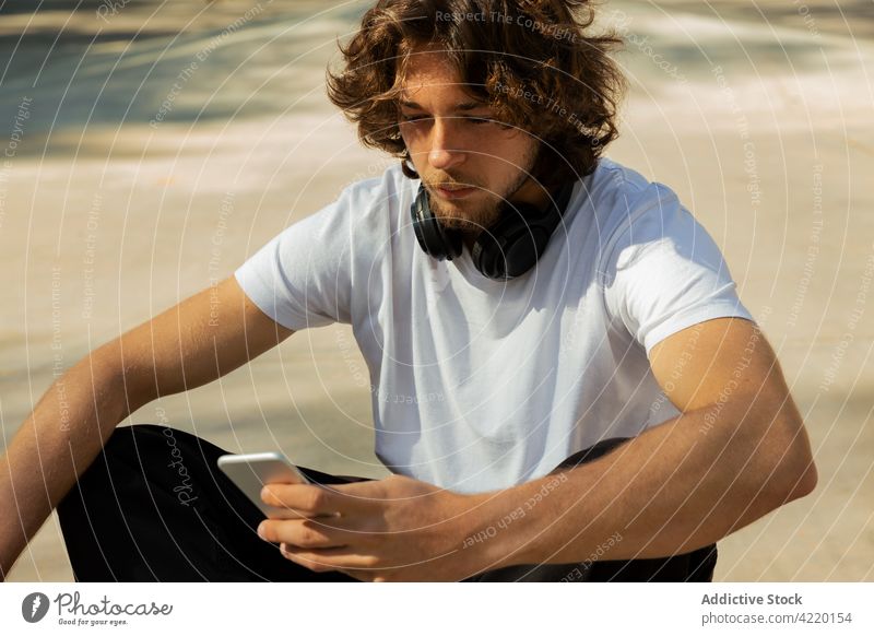 Portrait of a skateboarder looking at his phone Young man skating skatepark outside headphone cool horizontal cell recreation male slide people freestyle sport