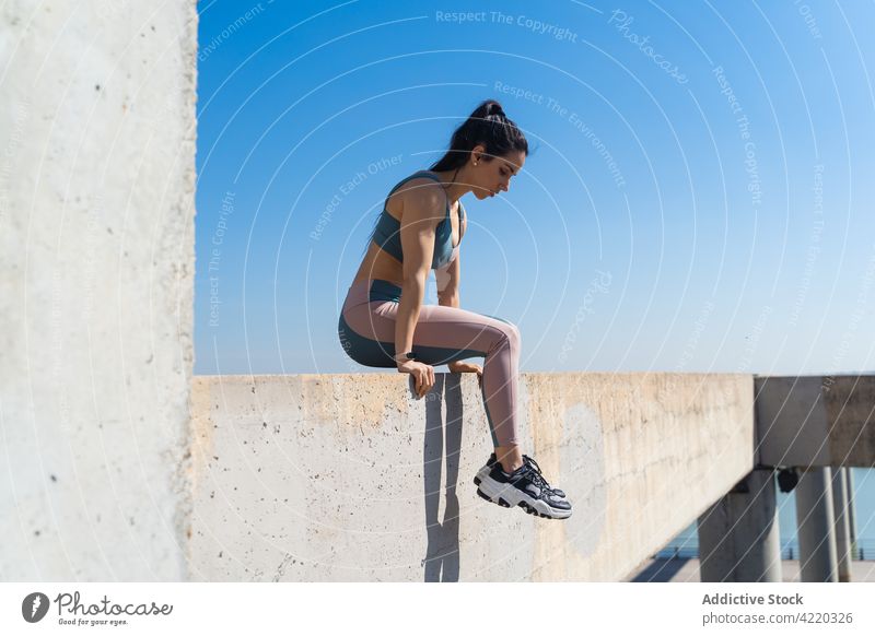 Sportswoman on concrete fence after workout outdoors sportswoman muscular sporty body strong wellness healthy lifestyle activewear blue sky break curve