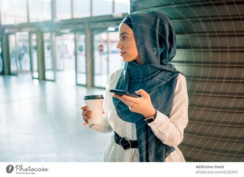Muslim woman browsing smartphone on train station railway station hijab wait takeaway drink female ethnic muslim cellphone mobile using internet watching gadget