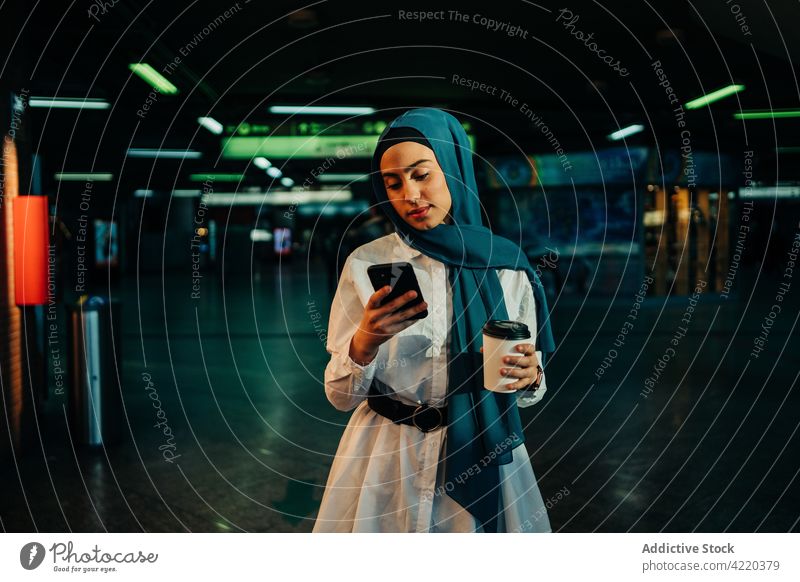 Muslim woman using smartphone in underground in city browsing takeaway drink surfing hijab female ethnic muslim mobile internet gadget headscarf connection