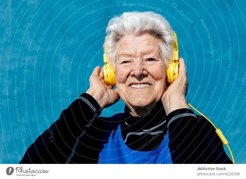 Cheerful senior woman listening to music in studio headphones song elderly smile enjoy sound female aged gray hair grandmother gadget device cheerful tune glad