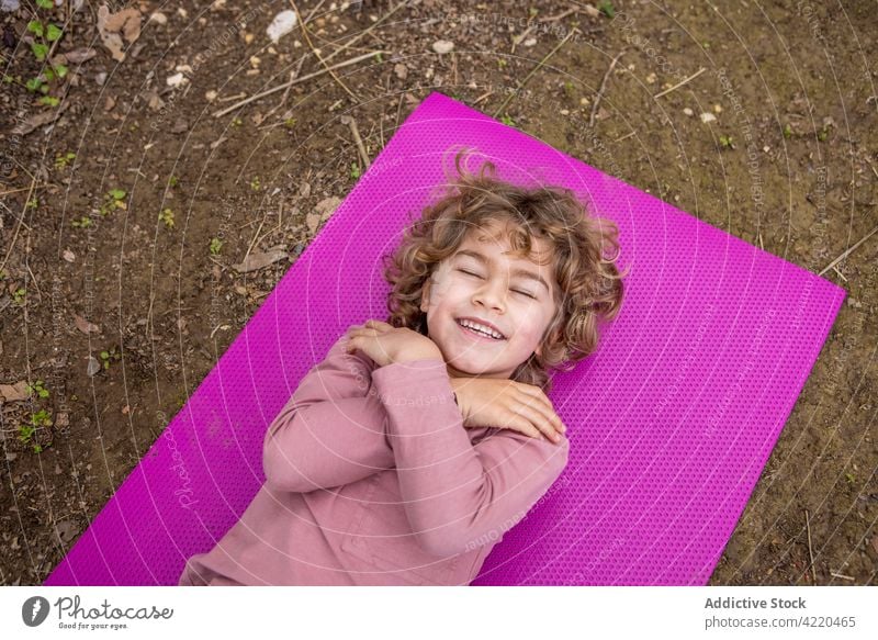 Cheerful boy with closed eyes resting on yoga mat arms crossed self regard eyes closed cheerful childhood portrait sincere mindfulness dreamy enjoy smile