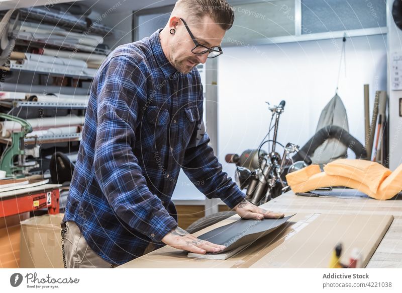 Bearded craftsman creating motorcycle seat upholstery at workbench workshop fabric cloth artisan hipster create master male creative material design focus