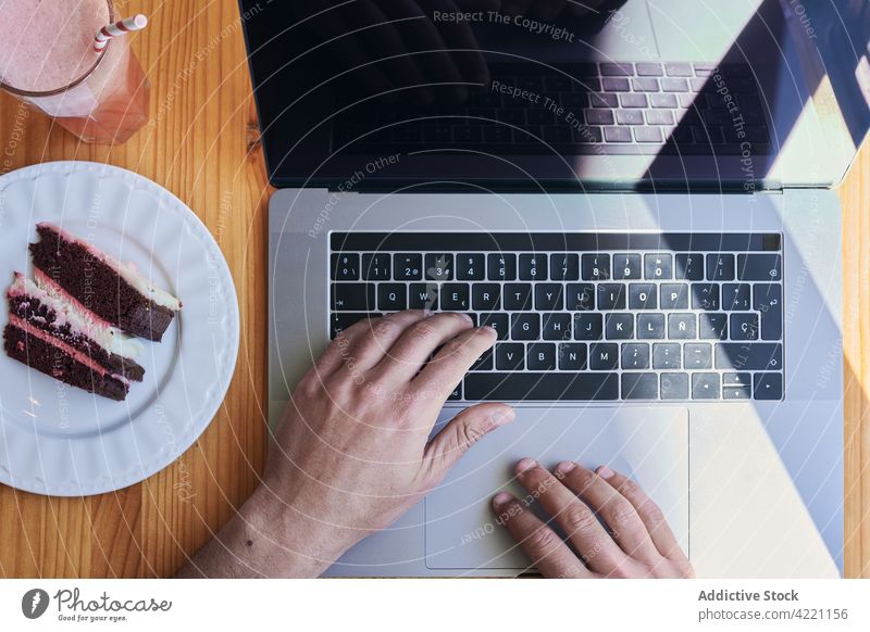 Crop freelancer typing on laptop at restaurant table with dessert employee black screen red velvet cake beverage using gadget device drink startup project
