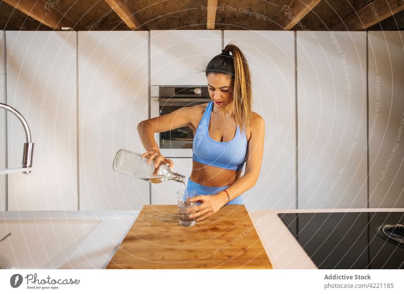 Athlete pouring water into glass in kitchen athlete bottle sporty vitality fresh woman sportswoman healthy lifestyle wellness feminine house pleasant process