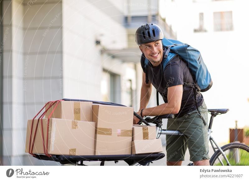 Bicycle messenger making a delivery on a cargo bike people young adult man male smiling happy blue collar Courier dispatch rider delivery man delivering package