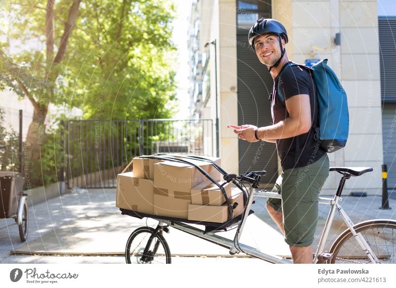 Bicycle messenger making a delivery on a cargo bike people young adult man male smiling happy blue collar Courier dispatch rider delivery man delivering package