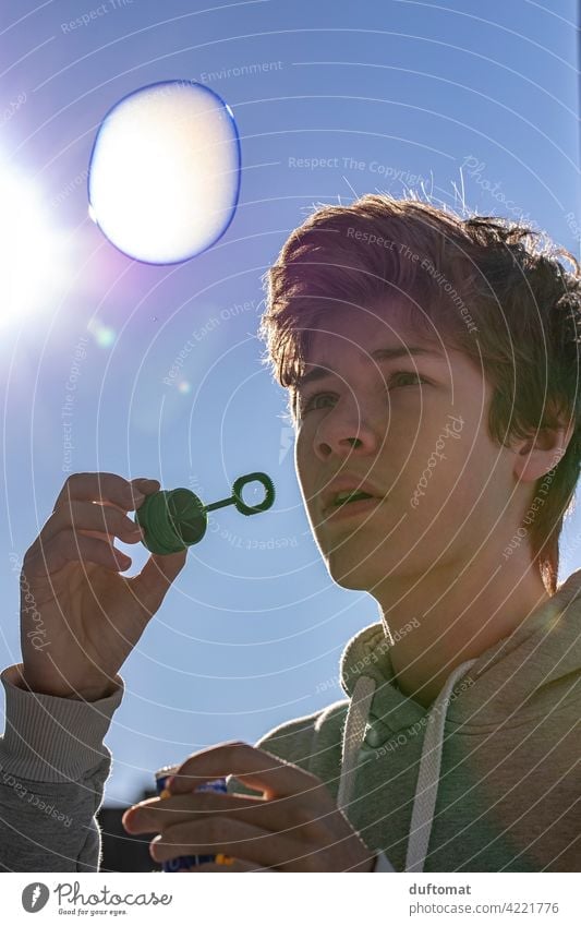 Teen boy blowing bubble in cold weather teenager Soap bubble Blow Joy Playing Infancy Colour photo Sky Flying Happy Dream Hover Bubble Exterior shot Freedom