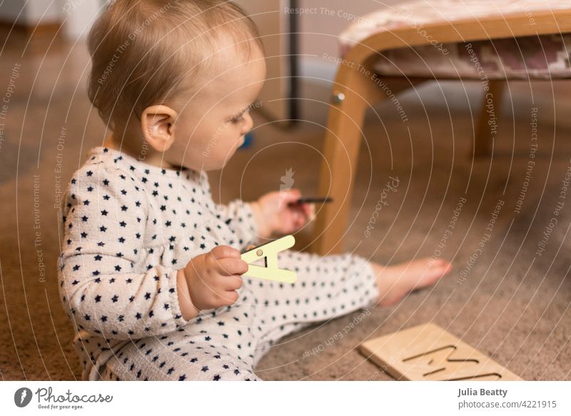 Ten month old toddler playing with a wooden letter puzzle on the floor child fine motor skills pincer 10 months old baby young grasp hold take off put on pull