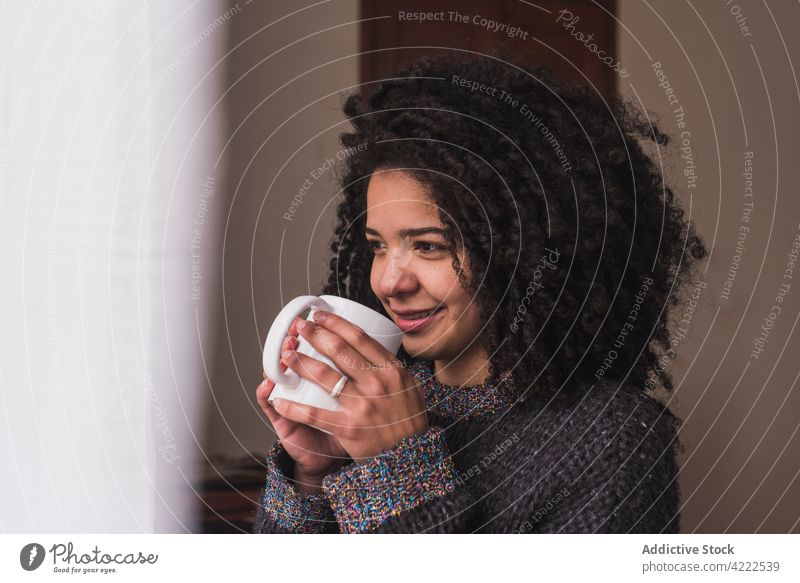Ethnic woman drinking beverage at home cup window smile afro hairstyle curly hair female ethnic charming dreamy enjoy hot drink cozy calm coffee tea mug