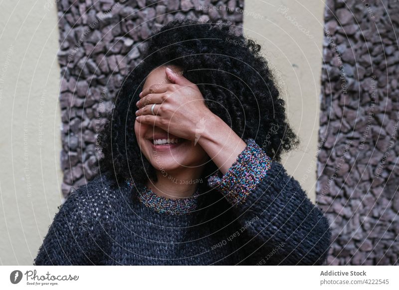 Happy ethnic woman with curly hair covering her eyes with her hand afro hairstyle smile charming appearance beauty natural female cheerful city young happy glad