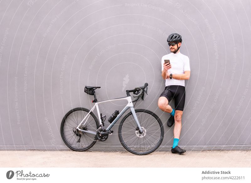 Bicyclist with smartphone against modern bike on gray background sport self assured leg raised style man urban gadget device cellphone sock shoe biker smile