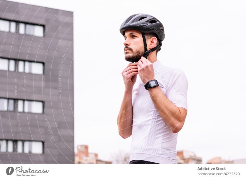 Cyclist putting on helmet on city street cyclist put on sport cycling smart watch fit masculine man town building protective macho virile biker modern style