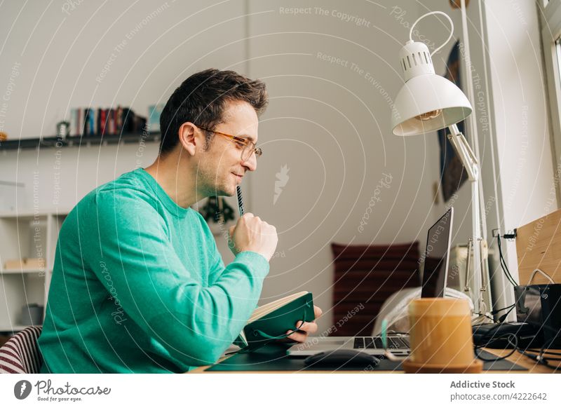 Smiling distance employee writing against laptop at home worker write freelance smile startup project man device gadget black screen reflection room lamp
