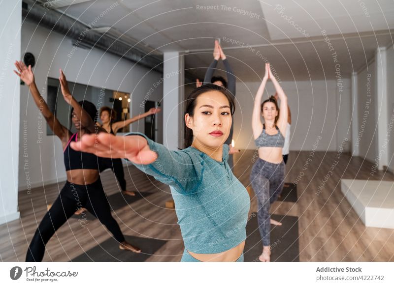 Asian woman doing yoga in Warrior pose during group lesson class people studio practice mindfulness warrior pose together multiracial multiethnic diverse asian