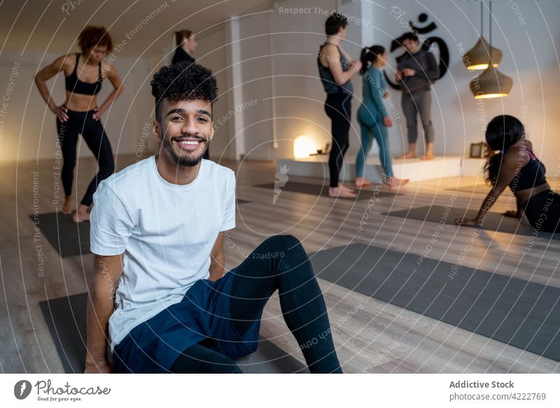 Cheerful black man sitting on mat in yoga studio class group lesson smile practice together cheerful multiracial multiethnic diverse african american healthy