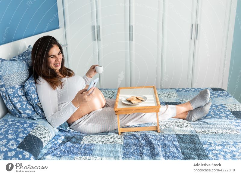 Happy pregnant woman having breakfast and browsing smartphone bed morning pregnancy watching phone call female home device happy cheerful bedroom sit gadget