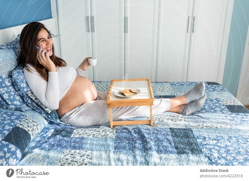 Happy pregnant woman having breakfast and talking on smartphone bed morning pregnancy speak phone call female home device happy cheerful bedroom sit gadget