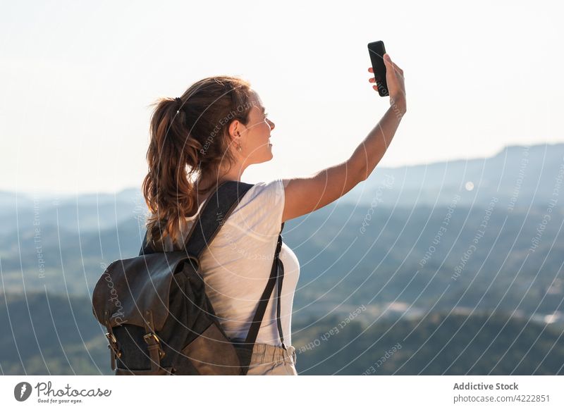 Content female traveler taking selfie on lush hilltop woman smartphone nature self portrait take photo content hiker backpacker cheerful mobile using device