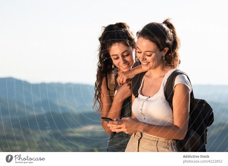 Cheerful women using smartphone on sunny hilly terrain friend together happy nature traveler cheerful gadget young browsing device toothy smile vacation surfing