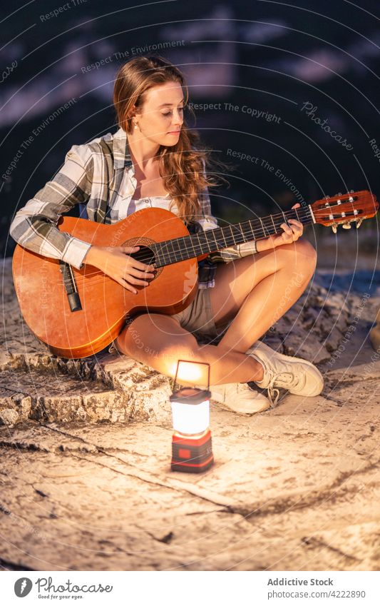 Traveler playing guitar in mountains in evening traveler woman music hiker player female lantern light glow nature sit rock enjoy tourist musician acoustic