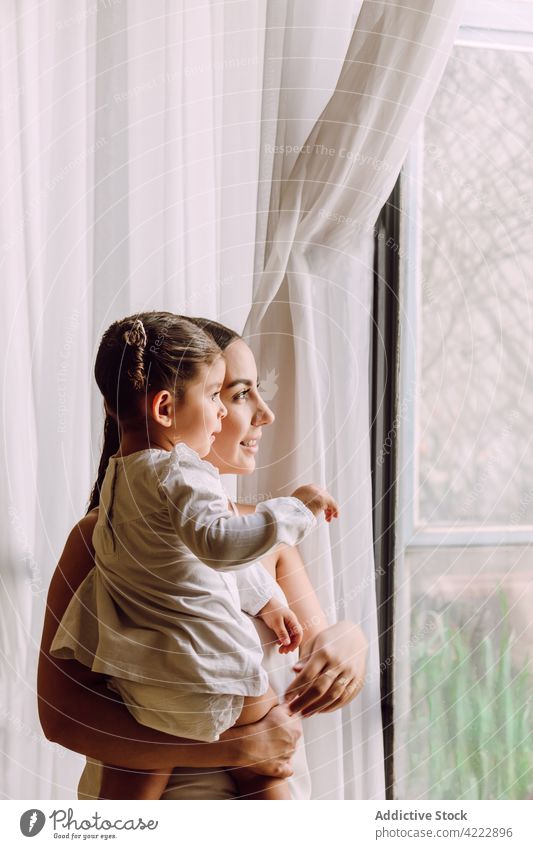 Woman with little child looking out of window mother home parent daughter curious interesting together ethnic kid at home girl mom adorable motherhood woman