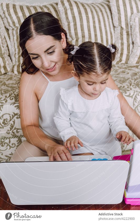 Mother and daughter watching movie on laptop mother child cartoon home little woman together ethnic sofa using girl kid gadget living room childhood internet