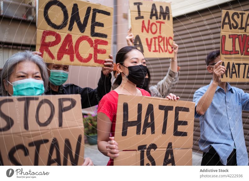 Asian protesters in face masks with placards on city street stop asian hate i am not a virus one race asian lives matter covid social hate is a virus racism