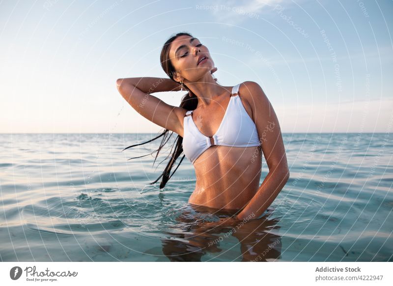 Sensual model in swimsuit in rippled ocean touch hair sensual body hand behind head feminine woman portrait wet hair sea swimwear white color confident seascape