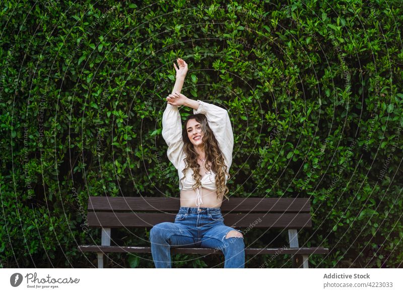 Happy young female sitting with arms raised on park bench woman cheerful toothy smile gorgeous verdant grace posture garden style content carefree happy