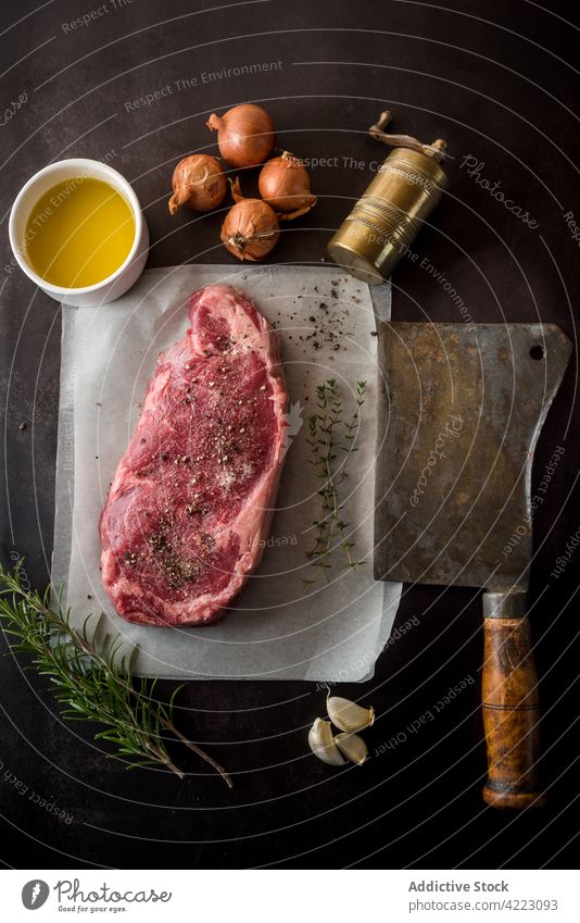 Raw beef steak with condiments against oil and fresh onions meat spice ingredient culinary recipe raw natural cleaver olive hatchet garlic rosemary thyme bowl