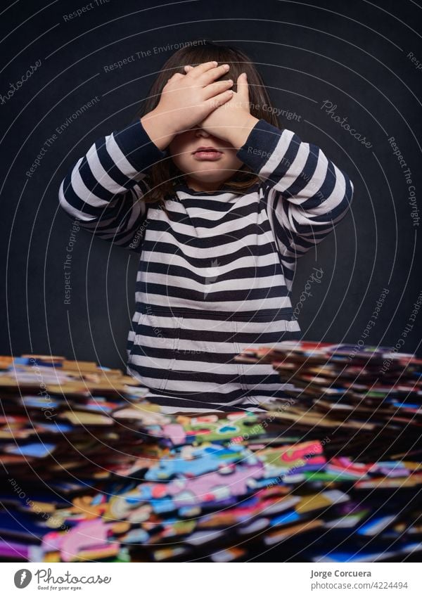 4 year old girl blocked with a lot of puzzle pieces covering her eyes with her hands . jigsaw toy board game kid play solve disorder construction solution