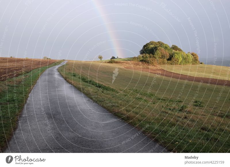 Lonely road through meadows and fields after the rain with a beautiful rainbow on the horizon in Gembeck at Twistetal in the district of Waldeck-Frankenberg in Hesse