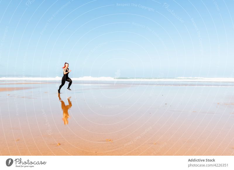 Fast runner jogging on sandy sea beach during workout jogger seashore sport training cardio activity tattoo woman reflection sportswoman exercise fast motion