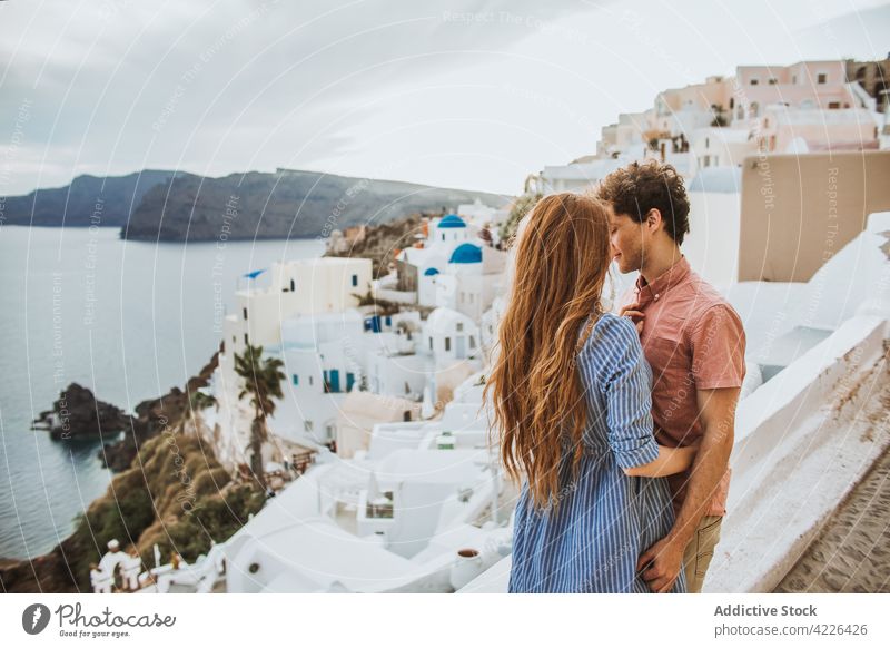 Young couple embracing on authentic coastal town street embrace traveler love romantic relationship seashore hug date holiday house affection resort oia village