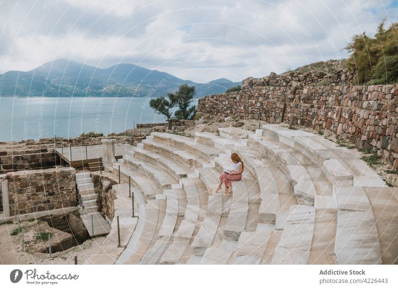 Unrecognizable woman reading book and sitting on ancient theater steps historic seashore heritage stair wanderlust plaka milos greece rest stone vacation summer