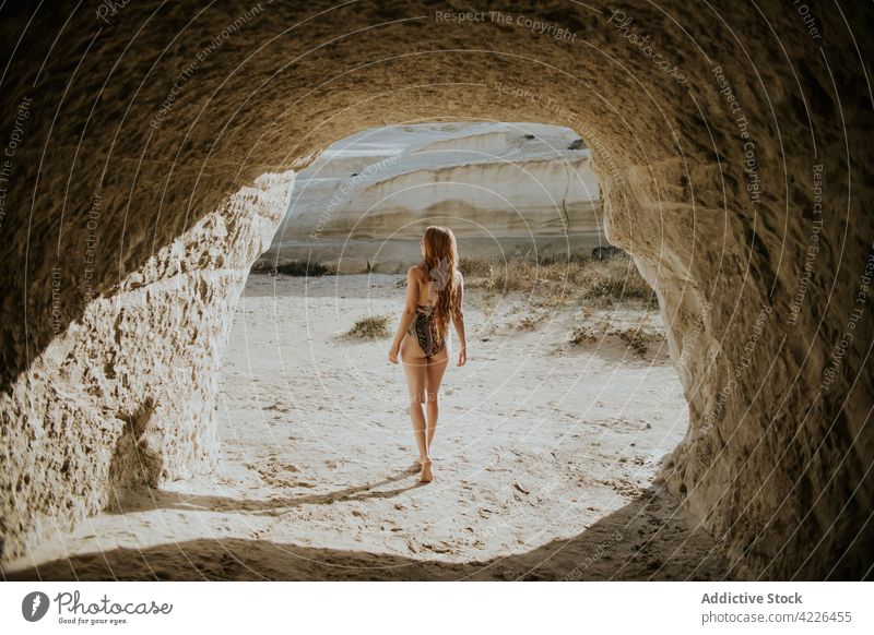 Anonymous woman in swimwear standing near stony cave travel fit sunny nature resort explore sunbath suntan sarakiniko formation milos greece vacation relax